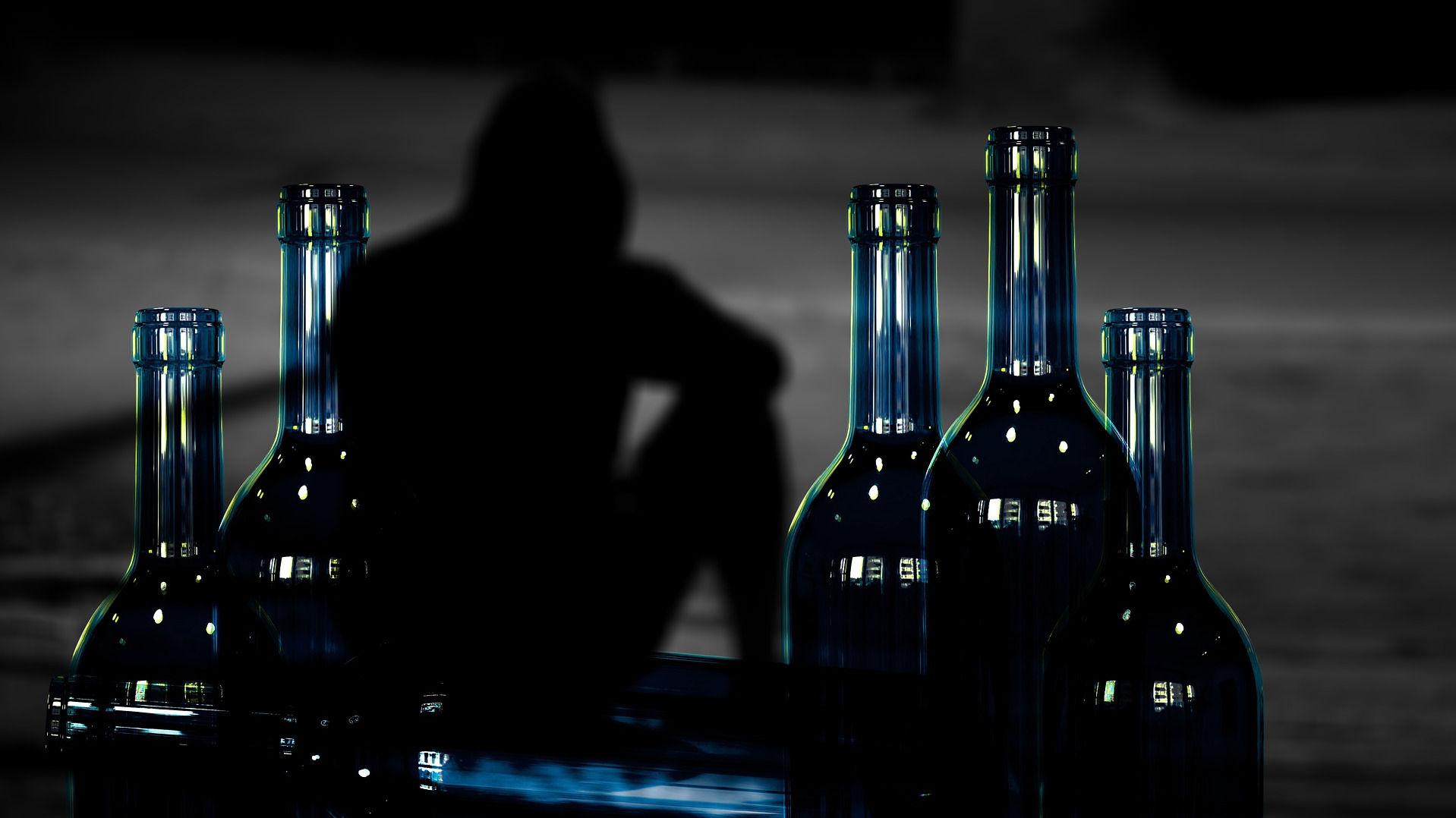 Man sitting in the shadows behind some bottles with alcohol